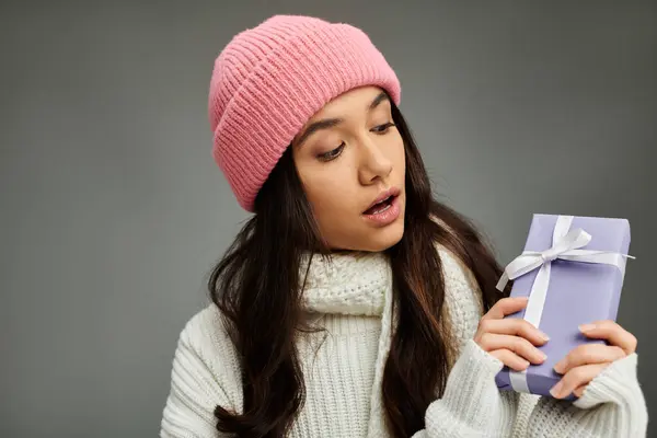 Die hübsche junge Frau sieht angenehm überrascht aus, während sie eine Geschenkbox in kuscheliger Winterkleidung in der Hand hält.. — Stockfoto