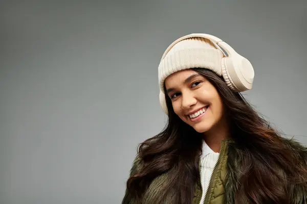 A vibrant young woman with a warm smile enjoys music while wearing fashionable winter clothing. — Stock Photo