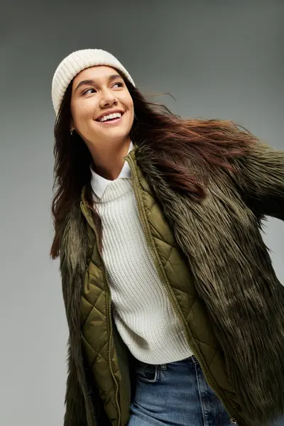 A young woman wearing a chic fur jacket and beanie radiates happiness in a minimalist setting. — Stock Photo