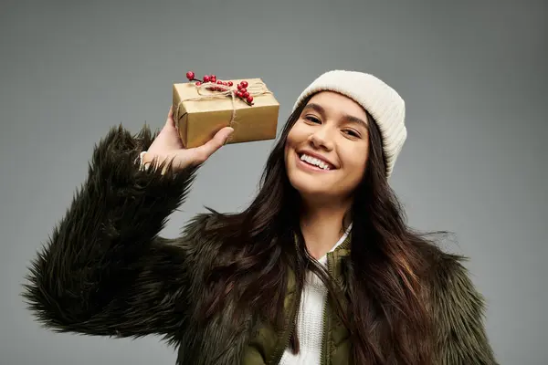 A cheerful young woman showcases a beautifully wrapped gift, radiating joy and warmth. — Stock Photo