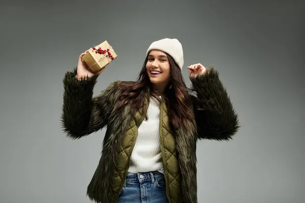 A young woman expresses joy while holding a beautifully wrapped gift in a warm outfit. — Stock Photo