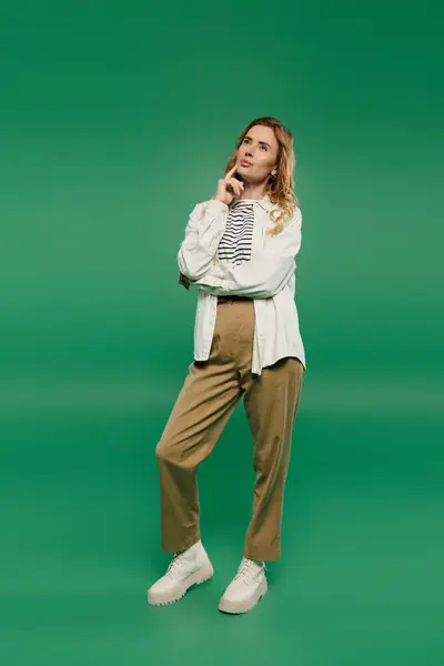 Curly-haired woman in casual attire thoughtfully poses against a bright green background. — Stock Photo