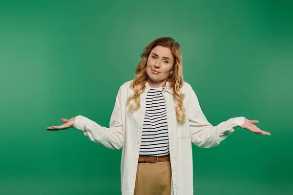 Una donna in abbigliamento casual alza le mani, trasmettendo un senso di confusione su uno sfondo verde brillante. — Foto stock