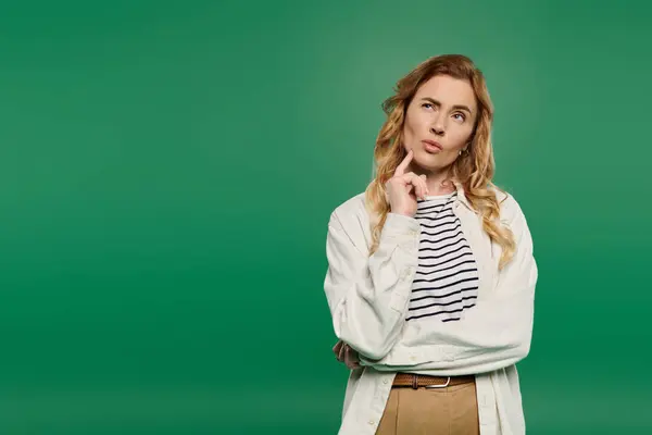 A beautiful woman in casual attire contemplates thoughtfully against a striking green backdrop. — Stock Photo