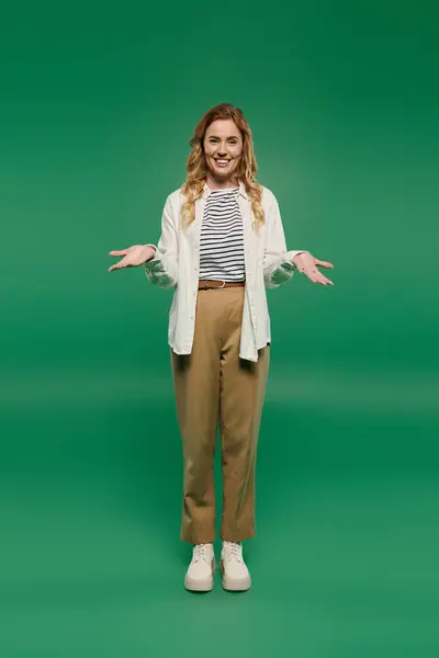 Eine fröhliche Frau mit lockigen Locken präsentiert ihren lässigen Stil vor leuchtend grünem Hintergrund, während sie gestikuliert. — Stockfoto