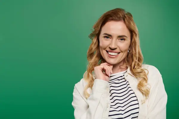 A cheerful woman with curly hair smiles warmly in casual clothes against a bright green background. — Stock Photo