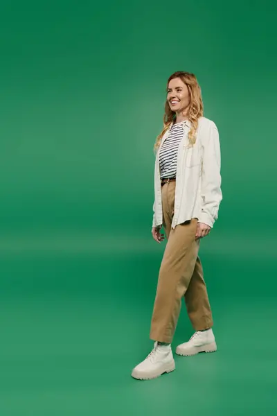 A woman with beautiful curly hair strolls casually in stylish clothes against a bright green backdrop. — Stock Photo