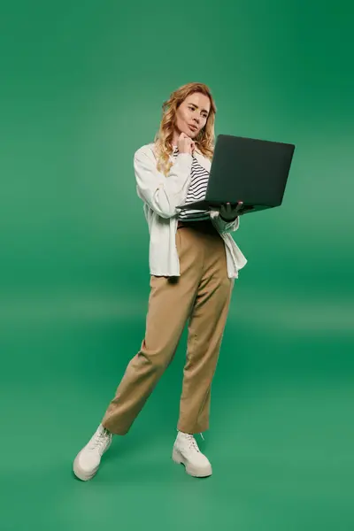 A casual woman with curly hair contemplates as she interacts with her laptop on a bright green background. — Stock Photo