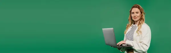 A stylish woman in casual attire engages with her laptop, exuding confidence in a refreshing green setting. — Stock Photo