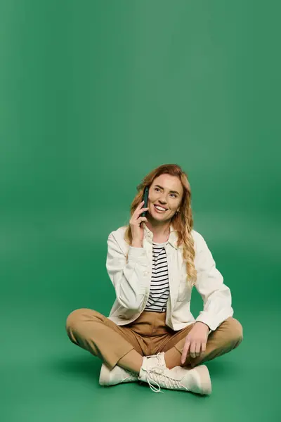 A smiling woman with curly hair casually chats on her phone while seated on the ground, radiating positivity. — Stock Photo
