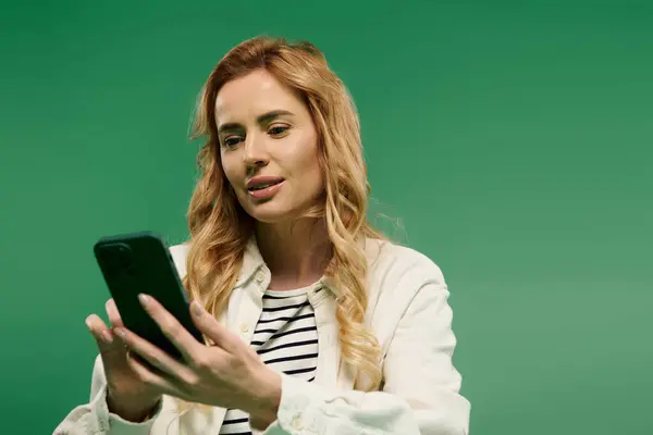 A stylish woman with curly hair enjoys her time looking at her smartphone on a bright green backdrop. — Stock Photo
