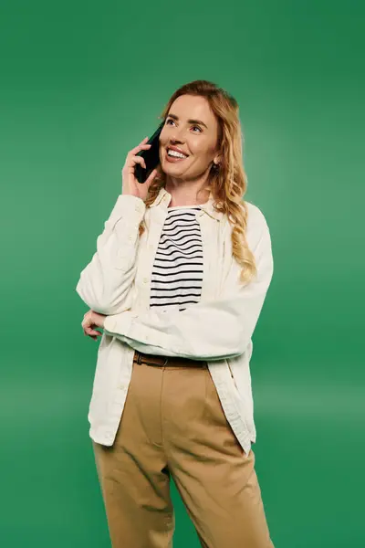 A cheerful woman with curly hair enjoys a phone conversation while wearing casual clothing on a bright green backdrop. — Stock Photo