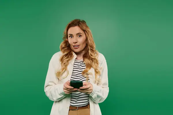 A woman with lovely curly hair enjoys using her smartphone, showcasing her relaxed style against green. — Stock Photo