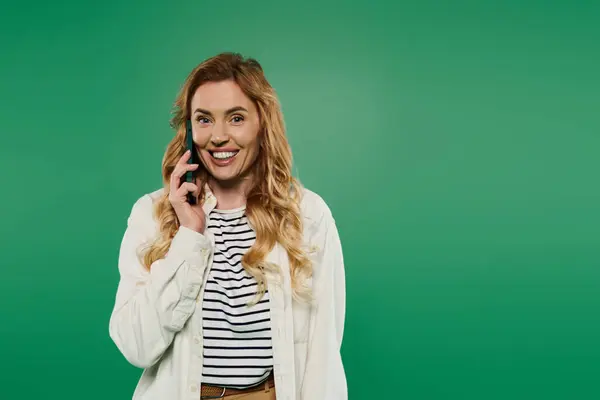 A cheerful woman with curly hair smiles as she talks on a phone, showcasing her casual style against greenery. — Stock Photo