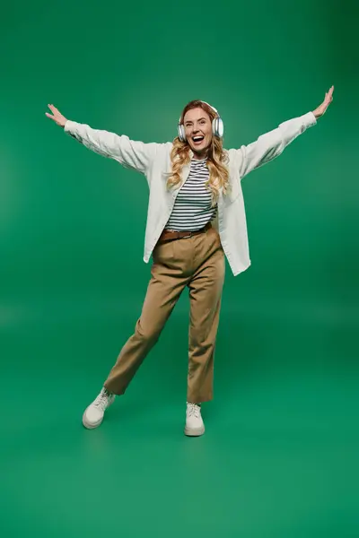 With a bright smile, a woman in casual attire joyfully dances while wearing headphones, immersed in music. — Stock Photo