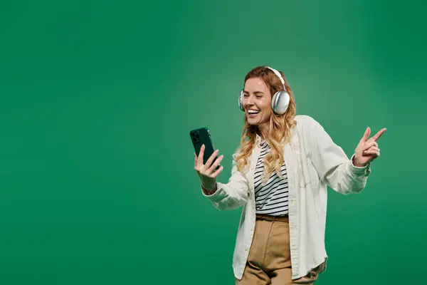 A cheerful woman with curly hair dances with joy while listening to music on her smartphone. — Stock Photo