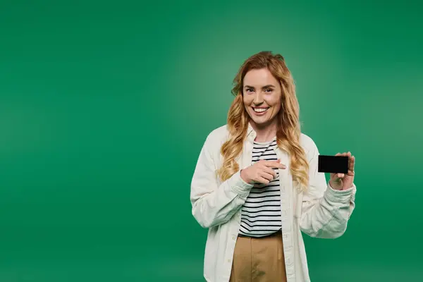 Uma mulher elegante sorri e aponta, segurando seu cartão brilhantemente contra um fundo verde exuberante. — Fotografia de Stock