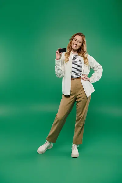 A joyful woman with beautiful curly hair stands confidently in casual attire, holding her card and smiling. — Stock Photo