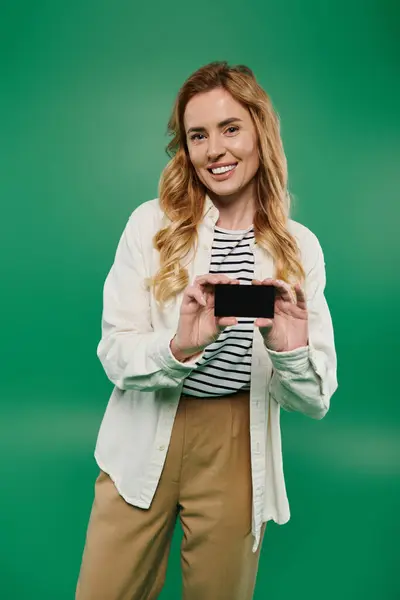 A woman with curly hair smiles brightly while holding a black card in front of a green background. — Stock Photo