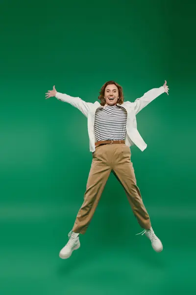 A cheerful woman with curly hair exudes happiness as she jumps on a bright green background, dressed casually. — Stock Photo