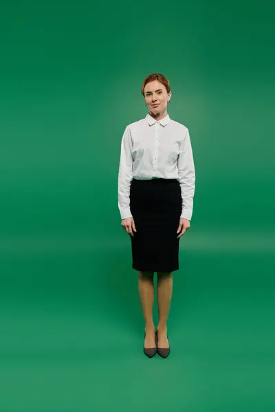 A confident woman in a white shirt and skirt poses against a green backdrop, ready for her call center role. — Stock Photo