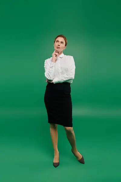 A thoughtful woman in a smart outfit stands against a vivid green backdrop — Stock Photo