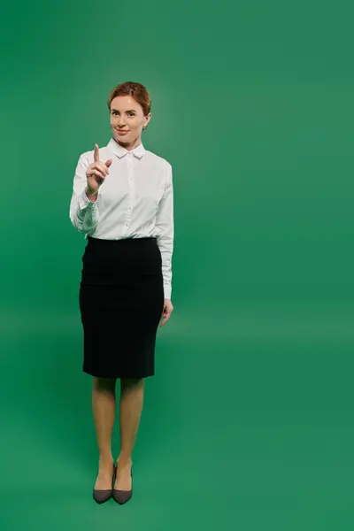 A poised woman in formal attire stands with a finger raised against a vibrant green backdrop — Stock Photo