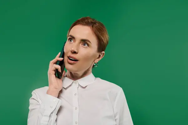 A confident woman in a white shirt connects on her smartphone, surrounded by a vibrant green backdrop. — Stock Photo
