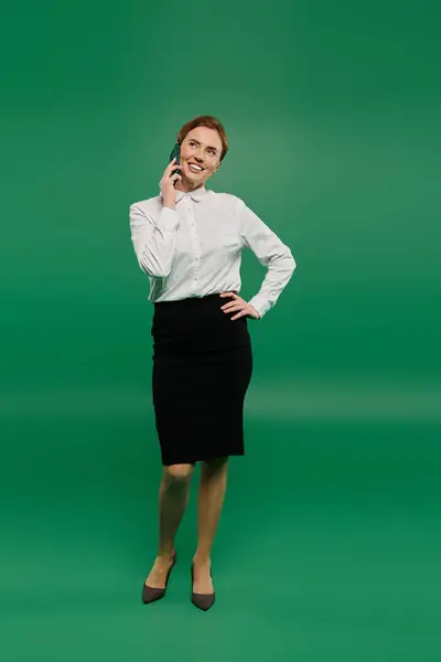 The woman in a white shirt and black skirt smiles while talking on the phone, showcasing professionalism. — Stock Photo