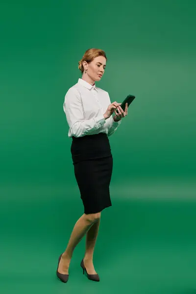 Une femme habillée professionnellement se tient prête, se concentrant sur son smartphone sur un fond vert accrocheur. — Photo de stock