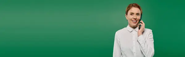 A confident woman in a white shirt speaks on the phone, set against a vibrant green backdrop. — Stock Photo