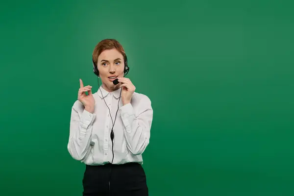 A professional woman wears a white shirt, engagingly speaking with a headset against a bright green background. — Stock Photo