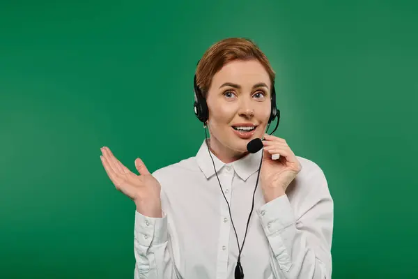 The woman in a white shirt enthusiastically communicates through her headset, set against a vibrant green backdrop. — Stock Photo