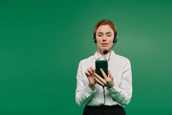 A confident woman in a white shirt uses her phone while wearing a headset in a vibrant environment. — Stock Photo