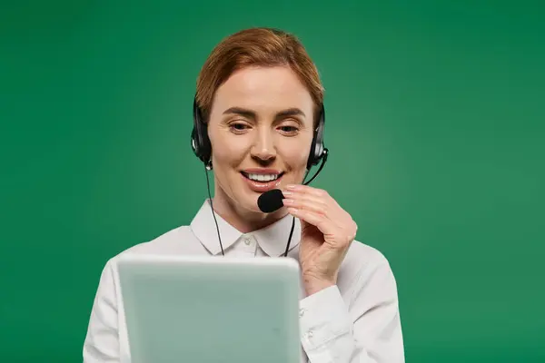A professional woman with a headset interacts enthusiastically during a call against a vivid green background. — Stock Photo