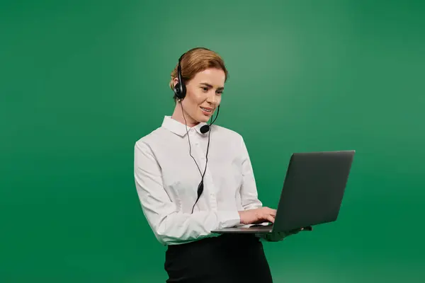 A confident woman in a white shirt communicates with clients while using a laptop and headset. — Stock Photo