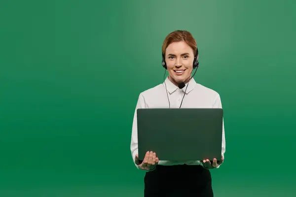 A confident woman in a white shirt holds a laptop, ready for call center interactions in a vibrant setting. — Stock Photo