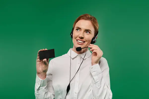 A professional woman smiles while holding a device, ready to assist clients in a vibrant call center setting. — Stock Photo