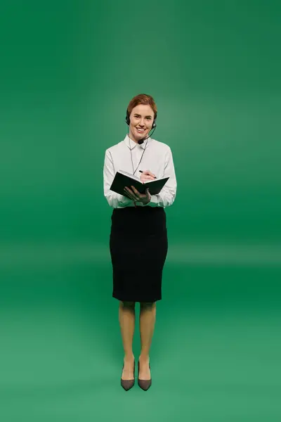 A skilled woman dressed in formal attire assists clients with a warm smile, standing against a green backdrop. — Stock Photo