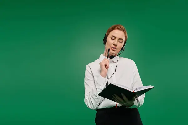 Une femme dévouée dans une chemise blanche prend des notes tout en utilisant un casque, dans un contexte vert vif. — Photo de stock