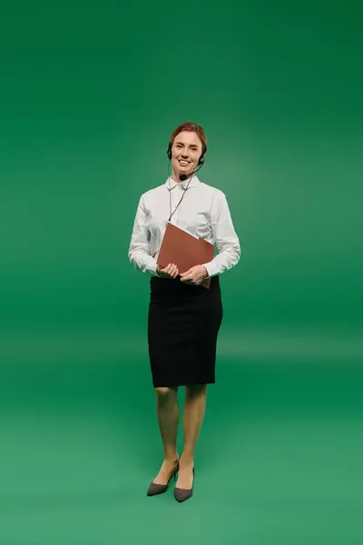 A smiling woman in a white shirt holds a folder while standing in a professional call center atmosphere. — Stock Photo