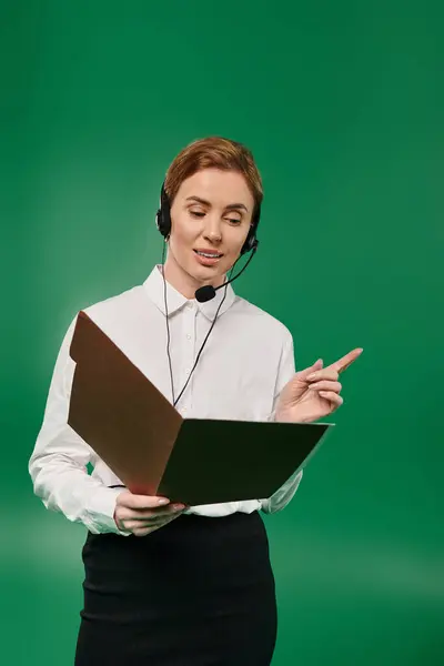 A woman in formal attire engages with clients while holding a document, set against a green backdrop. — Stock Photo