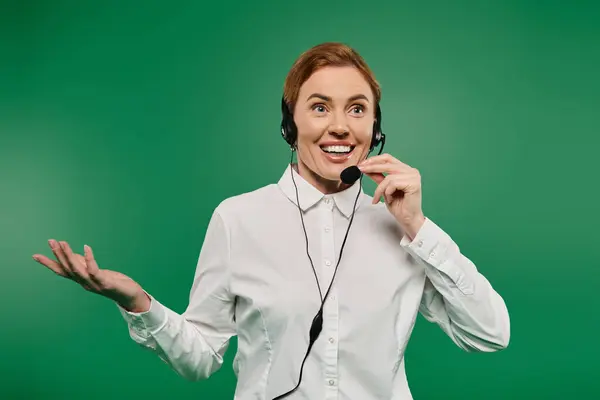 A woman in a white shirt communicates enthusiastically at a call center against a green backdrop. — Stock Photo