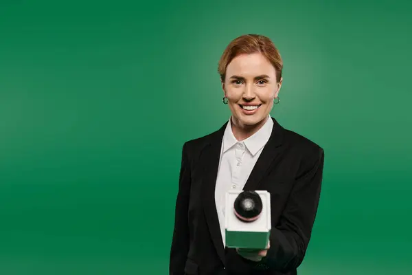 A confident TV presenter in elegant black attire stands on a vibrant green backdrop, engaging viewers with charisma. — Stock Photo
