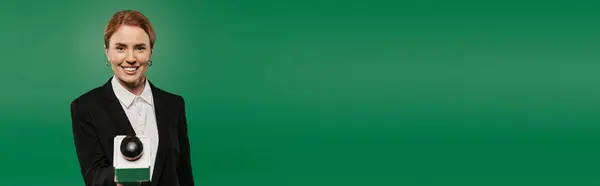 A poised TV presenter in black formal attire interacts with the camera against a striking green background. — Stock Photo