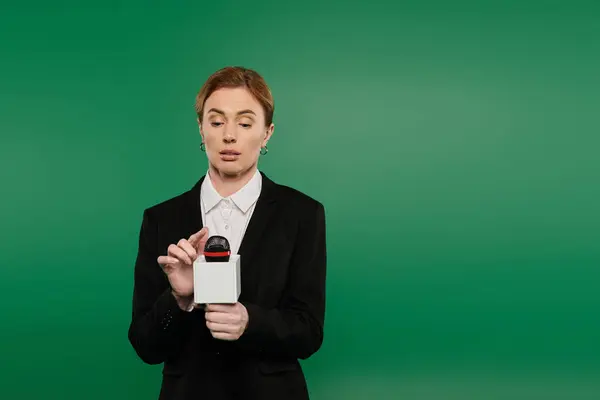 The TV presenter in stylish black attire engages with an audience while standing against a bright green background. — Stock Photo