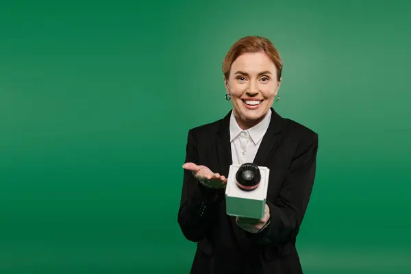 A charismatic TV host in black formal wear engages viewers against a vibrant green background. — Stock Photo