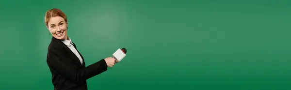 A dynamic TV presenter wearing black formal attire interacts enthusiastically against a bright green backdrop. — Stock Photo