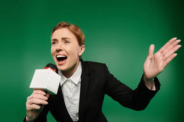 A dynamic presenter shares insights with a microphone, set against a vibrant green backdrop. — Stock Photo