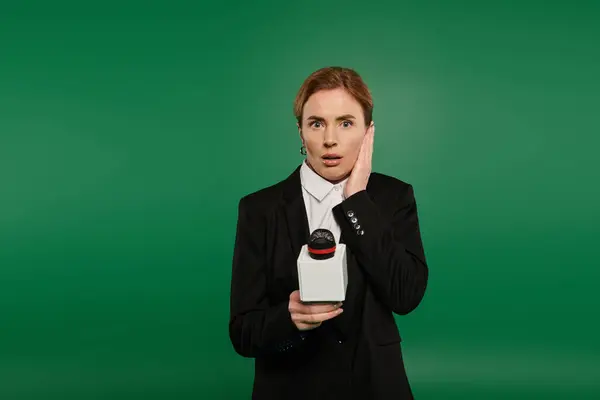 A TV presenter, dressed elegantly in black, reacts with surprise while standing against a vibrant green backdrop. — Stock Photo
